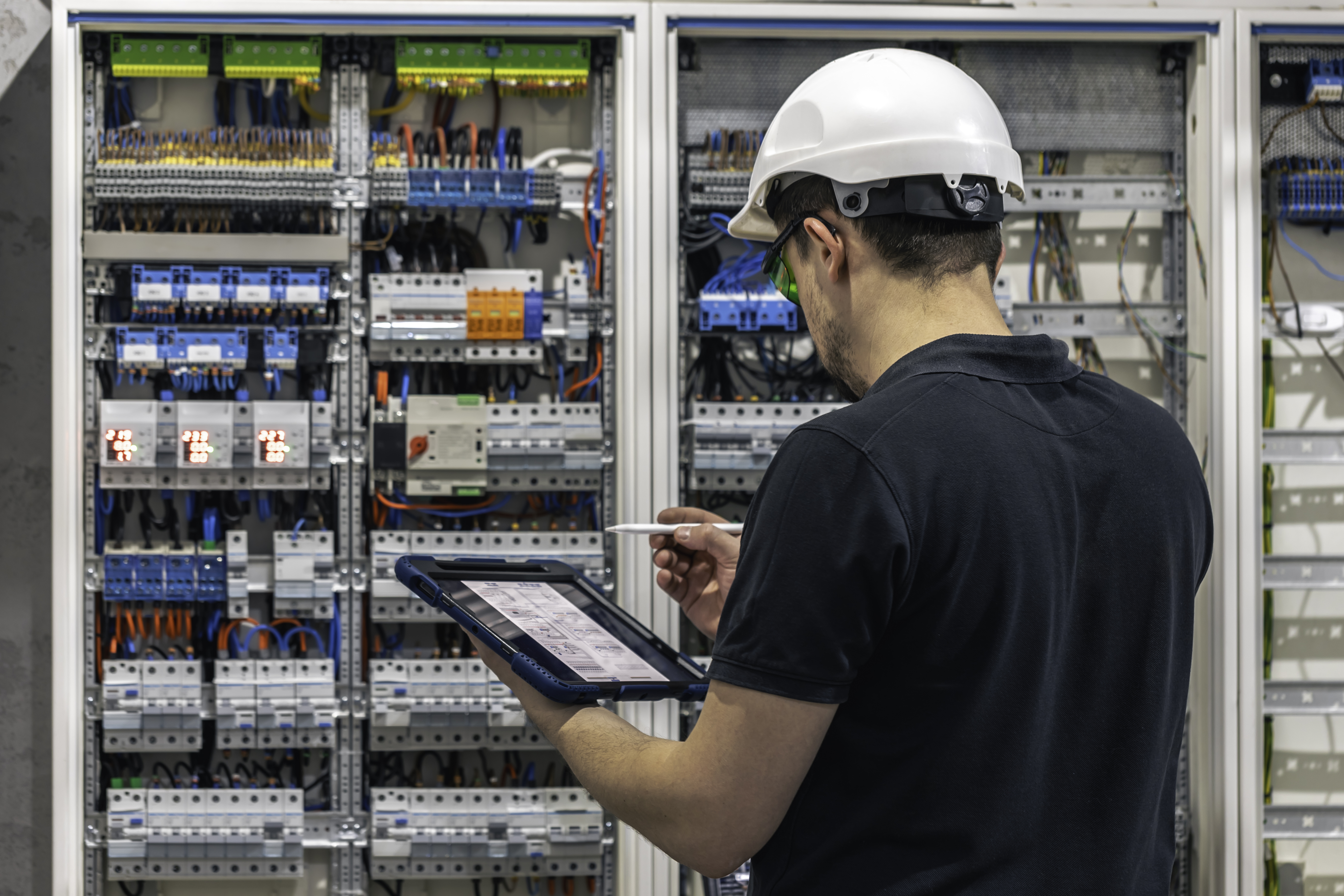 Man an electrical working in a switchboard with fuses uses a tablet
